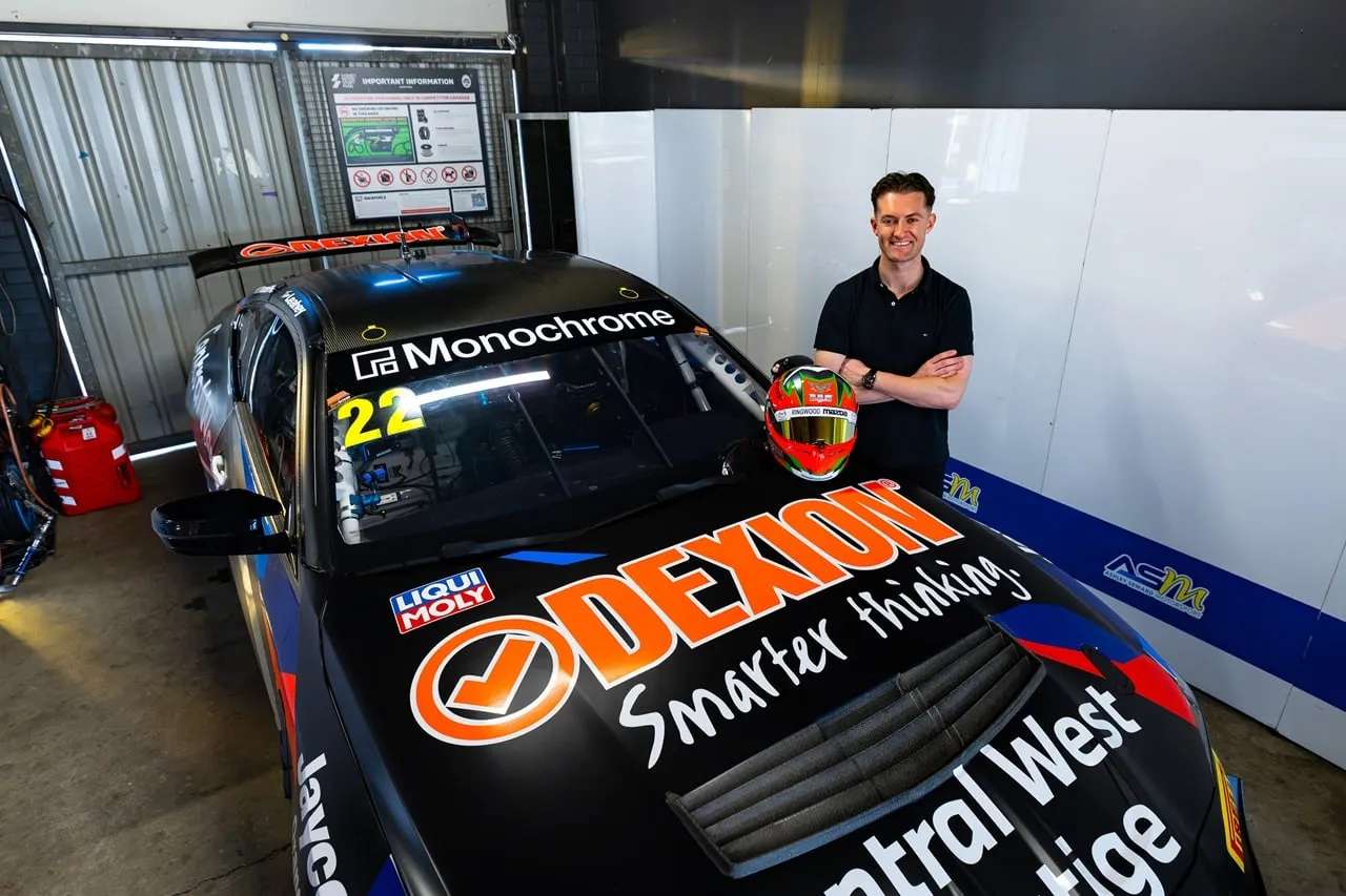 Dylan O'Keeffe standing arms folded beside a Dexion-liveried race car in the garage