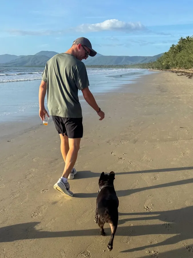 A man in a cap walking a dog along a beach